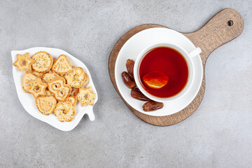 A plate of biscuits and a cup of tea with dates on saucer on wooden board on marble background