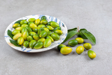 Kumquats and leaves on an ornate plate and on marble background