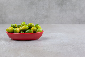 Kumquats in a red oval bowl on marble background