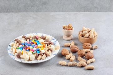 Plate of candies and chocolate mushrooms with scattered bowls of peanuts and walnuts on marble background