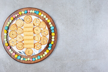 Plate of assorted cookies encircled by popcorn candy on wooden board on marble background
