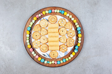 Plate of assorted cookies encircled by popcorn candy on wooden board on marble background