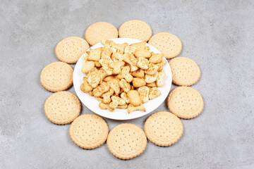 Plate full of cookie chips surrounded by biscuits on marble background