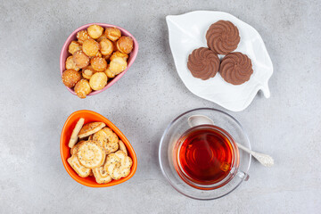 Obraz na płótnie Canvas Few cookies on plate next to bowls of cookie chips and a cup of tea on marble background