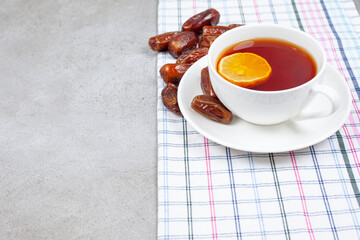 A cup of tea on saucer next to dates on towel on marble background