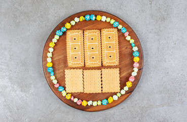 Biscuits surrounded by candies in a circle on wooden board on marble background
