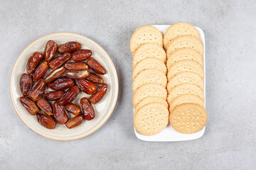 Plate of dates next to plate of biscuits on marble background