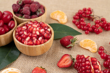 Bowls of pomegranate, raspberries and hips with scattered assortment of fruits on textile background