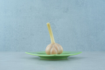 Plate of raw garlic on gray background
