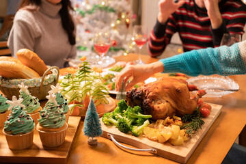 Selective focus of Christmas dinner on table with hand put a small Christmas tree next to a roasted turkey with broccoli and potatoes, easy appetizer, Christmas tree cupcakes, breads on Christmas Eve.