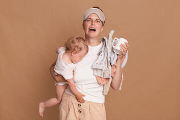 Horizontal shot of desperate sad frustrated mother with baby daughter and laundry in hands, being...