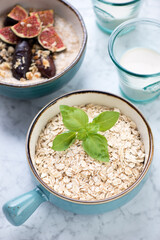 Turquoise bowl with oat flakes on a light-grey marble background, vertical shot, selective focus
