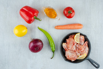 Pan of seasoned chicken, oil and vegetables on stone surface
