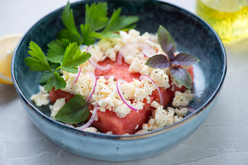 Close-up of watermelon served with feta cheese, fresh parsley and basil in a blue bowl, selective focus, horizontal shot