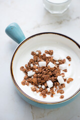 Greek yogurt with chocolate granola and coconut in a turquoise serving bowl, vertical shot on a beige marble background, middle closeup