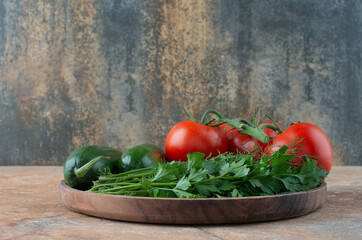 A wooden plate with cucumbers, greens and tomatoes