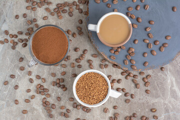 Cup of coffee, coffee beans and ground coffee on marble surface