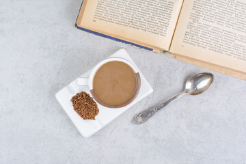 Cup of milk coffee, spoon and book on stone surface