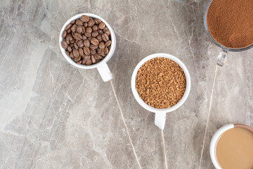 Cup of coffee, coffee beans and ground coffee on marble surface