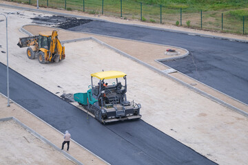 Worker, asphalt paving machine  while lays asphalt and excavator on construction site, top view