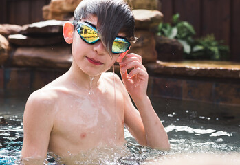 a boy swimmer in the backyard inground swimming pool wearing goggles touching ear