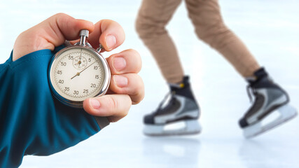 measuring speed on skates with a stopwatch. hand with a stopwatch on the background of the legs of a man skating on an ice rink