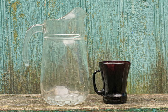 a set of dishes from a large empty white glass jug and a brown cup stand on a gray table against a green wall