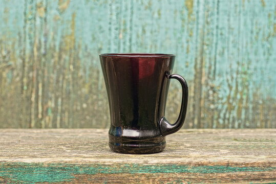 one large glass brown cup stands on a gray table against a green wall