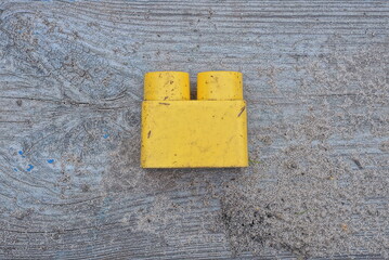 one yellow small plastic part from a toy constructor lies on gray sand on a wooden table in the street