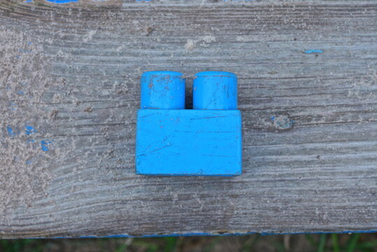 one blue small plastic part from a toy constructor lies on gray sand on a wooden table in the street
