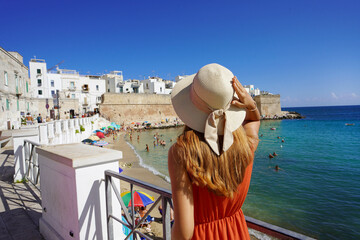Summer holiday in Italy. Back view of young woman with hat and dress enjoying seascape in Monopoli...