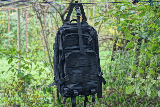 one big black army backpack hangs on a wire in the street among the vegetation