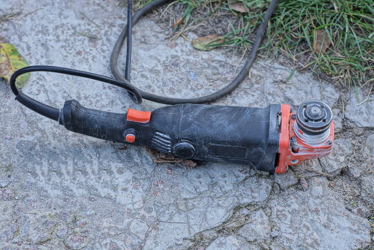 one power tool from a black red grinder lies on gray concrete in green grass on the street