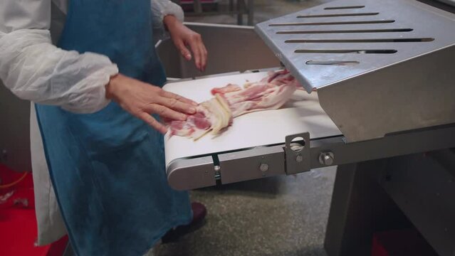A meat factory worker puts unprocessed pieces of meat into a skinning machine