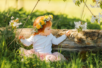 Cute little girl is wearing beautiful spring wreath outdoors, space for text. Red hair baby is...