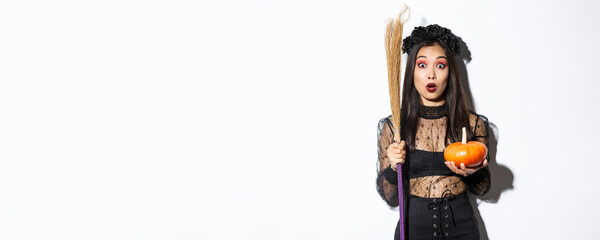 Image of surprised asian girl gasping wondered and stare at camera, wearing witch costume on...