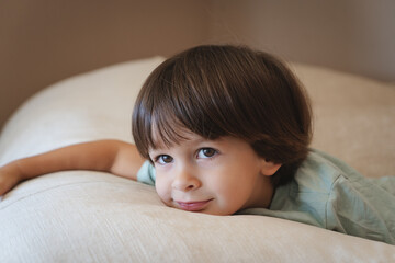 Cute little boy looking in the camera while lying on the sofa close up