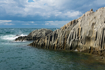rocky seashore formed by columnar basalt against the surf, coastal landscape of the Kuril Islands