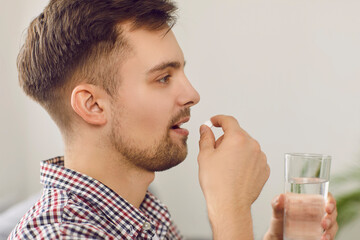 Side view of a man taking medicine. Profile closeup shot of a happy young Caucasian man taking a pill with a glass of clean water. Medication, health, undergoing treatment concepts - Powered by Adobe