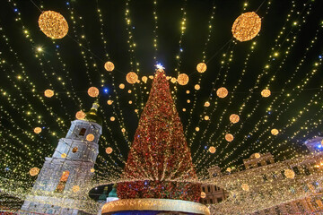 Illuminated Christmas tree with garlands against night sky. Bell tower of St Sophia Cathedral on...