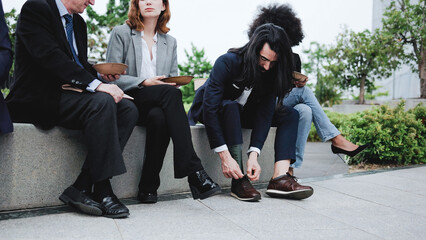Fototapeta premium Business man with physical disability adjusting leg prosthesis during lunch break with colleagues outside the office - Focus on hands