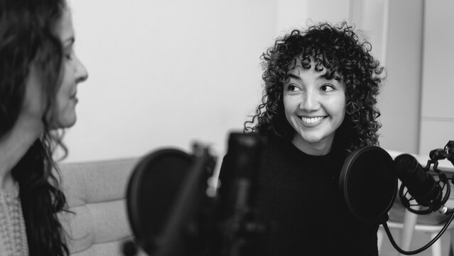 Female host recording radio podcast interview with guest at home office - Focus on latin girl face - Black and white editing