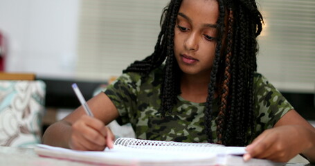 Black teen girl doing homework at home writing paper studying