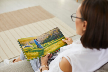 Senior woman looking through pictures in printed family album. Mother enjoying romantic photoshoot...