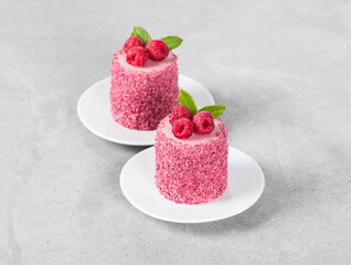 Raspberry mousse cake of cylindrical shape, on a plate. Light grey background	