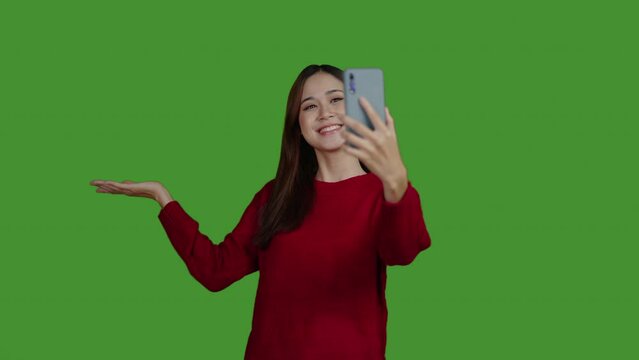  Footage of happy woman in red sweater is talking on cell phone or taking a selfie photo. Indoor isolated on green background.