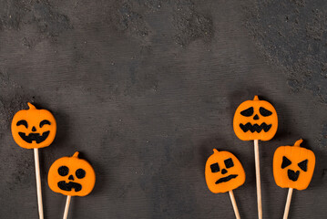Halloween holiday. Creamy jelly candies in the shape of a pumpkin, on a wooden stick. Dark background. Top view. Copy space	
