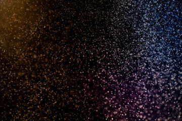 Fototapeta na wymiar Dust particles floating on a colorful rainbow light on black background. Glittering sparkling flickering overlay.