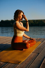 A calm woman sits in a lotus yoga pose and practices breathing exercises.
