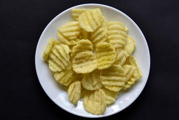Delicious peppery corn chips on a white plate. Beer appetizer on a plate on a black background.